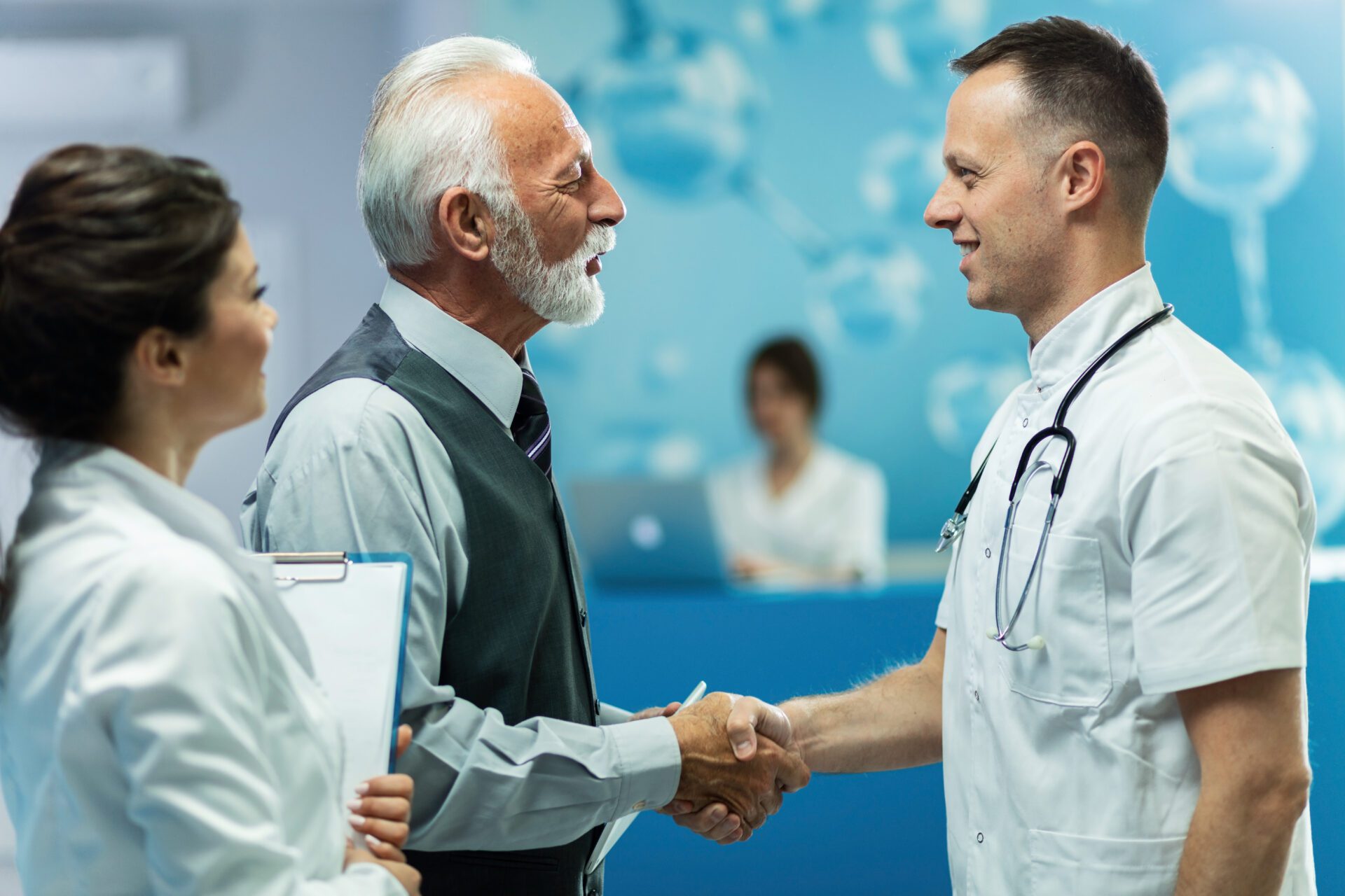 Happy senior man and male doctor handshaking while greeting in a hallway at clinic. Happy senior man and male doctor handshaking while greeting in a hallway at clinic.